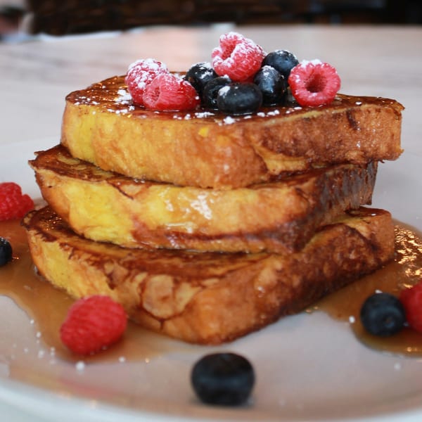 Stack of three golden French toast slices, drizzled with syrup, topped with raspberries and blueberries.