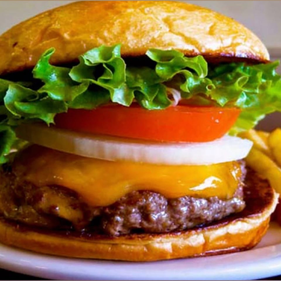 A Moish and Itzy's cheeseburger with lettuce, tomato, onion, and melted cheese on a bun.
