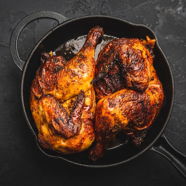Two golden-brown roasted chicken halves in a black cast iron skillet, from Moish and Itzy’s.