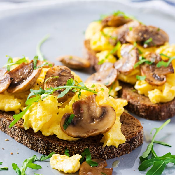 Scrambled eggs and sliced mushrooms on dark rye toast, garnished with arugula.