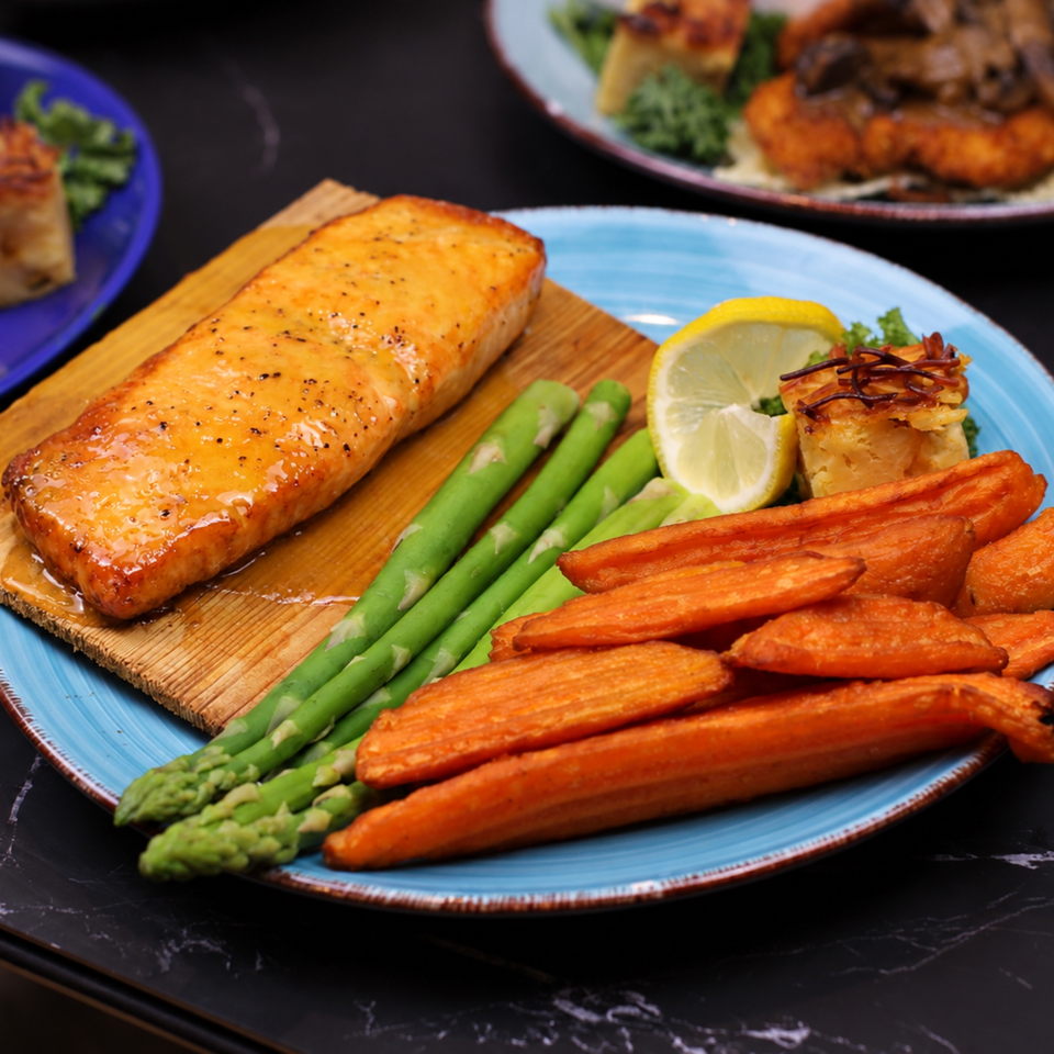 Glazed salmon fillet with roasted carrots, asparagus, lemon, and a vegetable pastry on a blue plate.