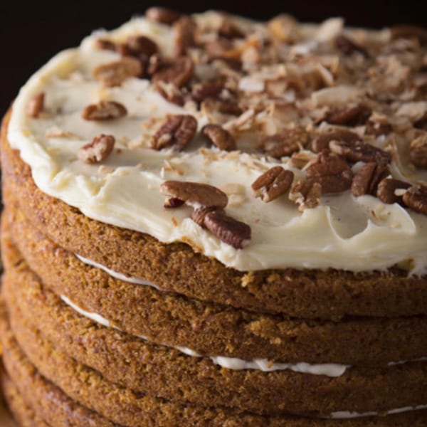 Close-up of a multi-layered carrot cake with white frosting and chopped pecans on top.
